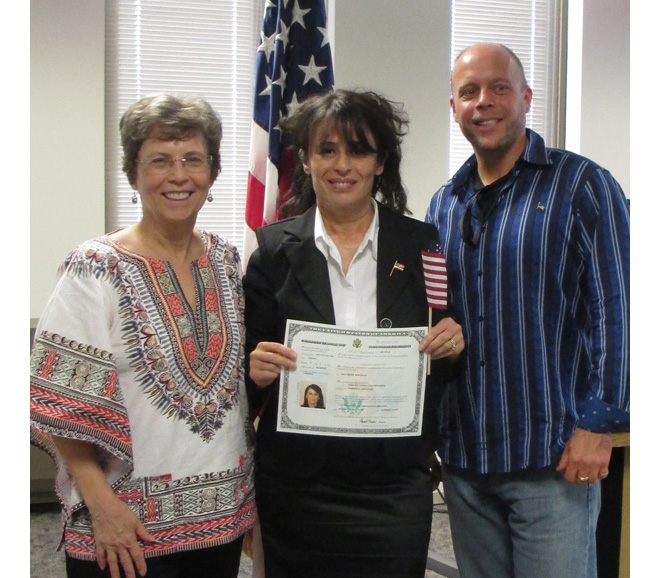 Dona stands with her son Paul and his wife Jomania in front of an American flag.  Jomania is holding her new certificate of citizenship.